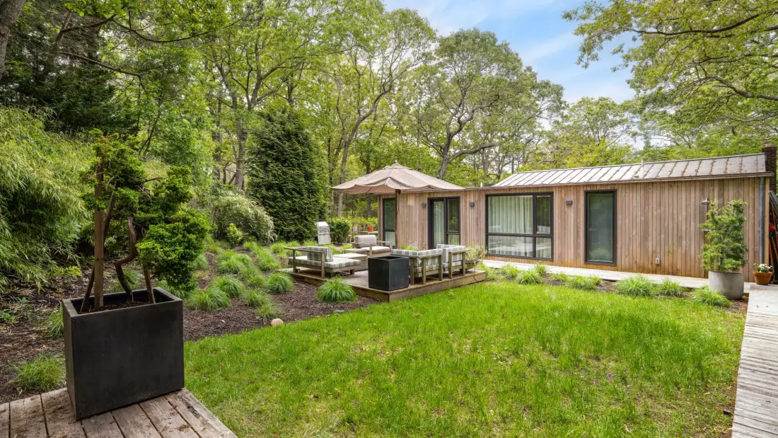 A garden lawn beside a low wooden building, with trees and patio seating.