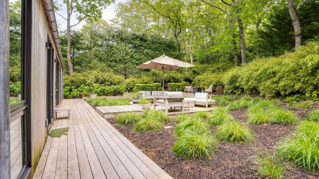A wooden deck beside a garden seating area with a patio umbrella and greenery.