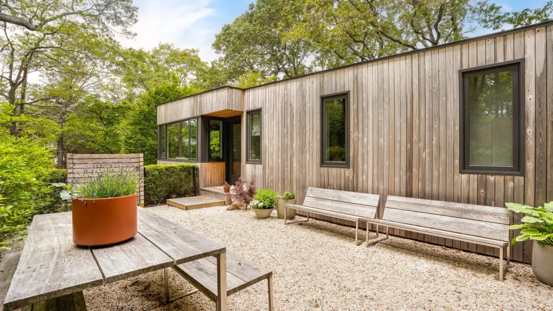 Un patio exterior junto a un edificio revestido de madera, con bancos y plantas en macetas.