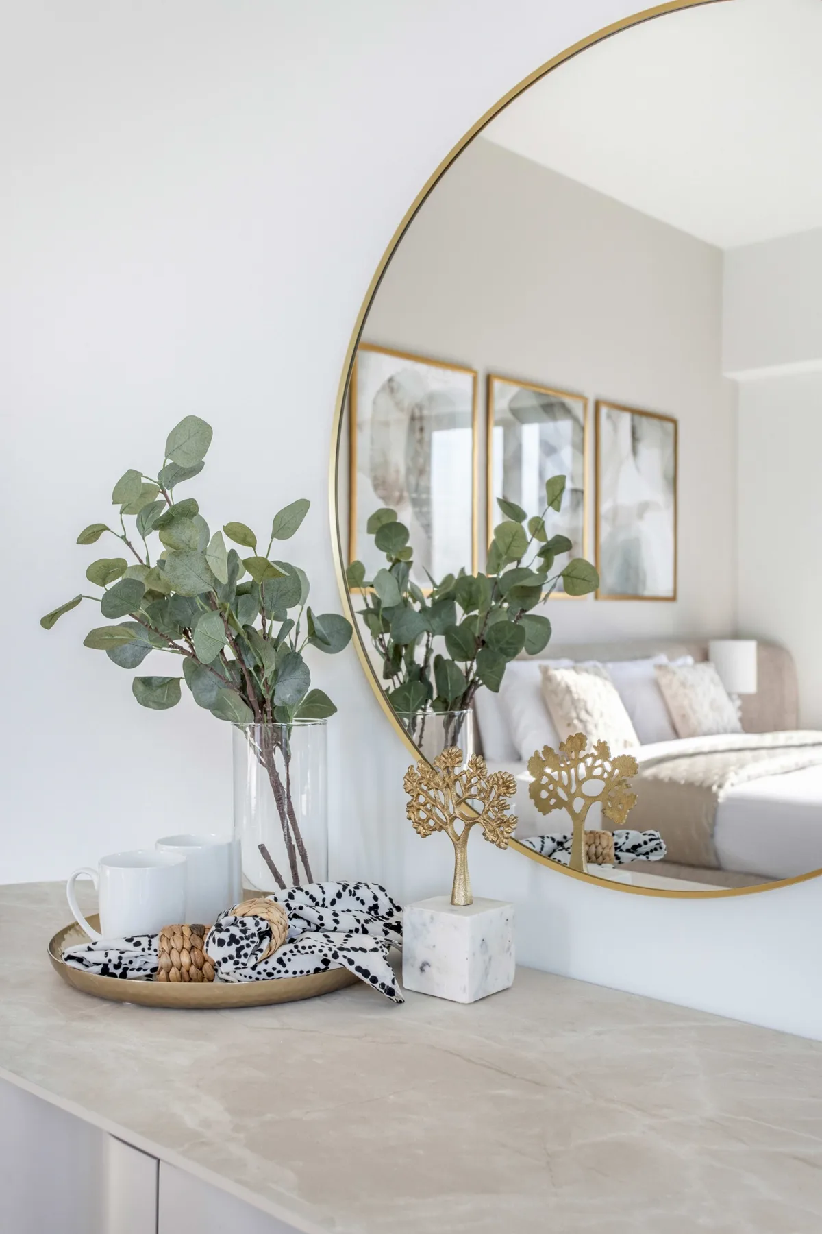 Un dormitorio reflejado en un espejo redondo sobre una cómoda de color claro.