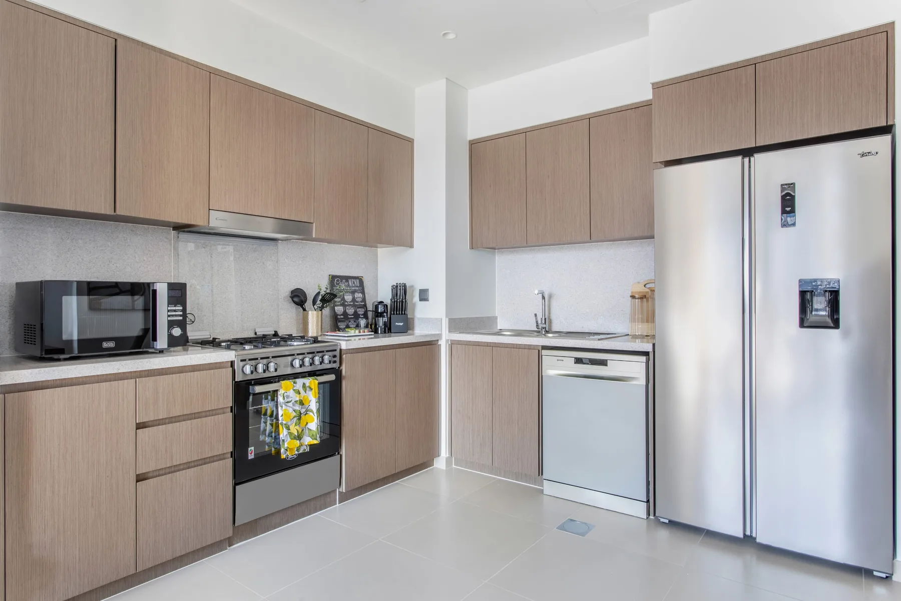 Una cocina moderna con gabinetes en tonos de madera, electrodomésticos de acero inoxidable y piso de baldosas claras.