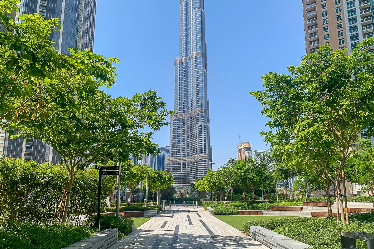 Un parque urbano ajardinado con un sendero pavimentado, árboles y edificios altos.