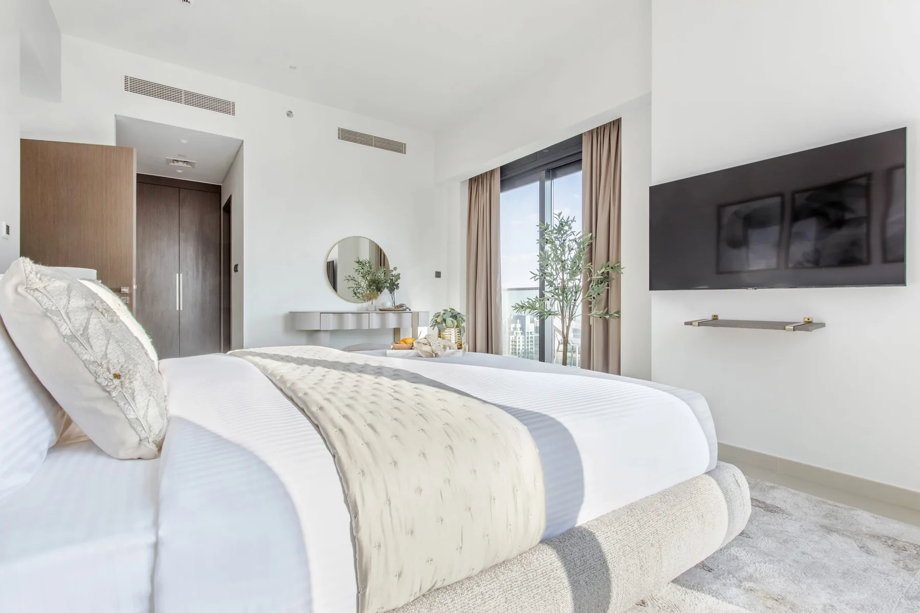 Un dormitorio luminoso con una cama bien tendida y un televisor en la pared.
