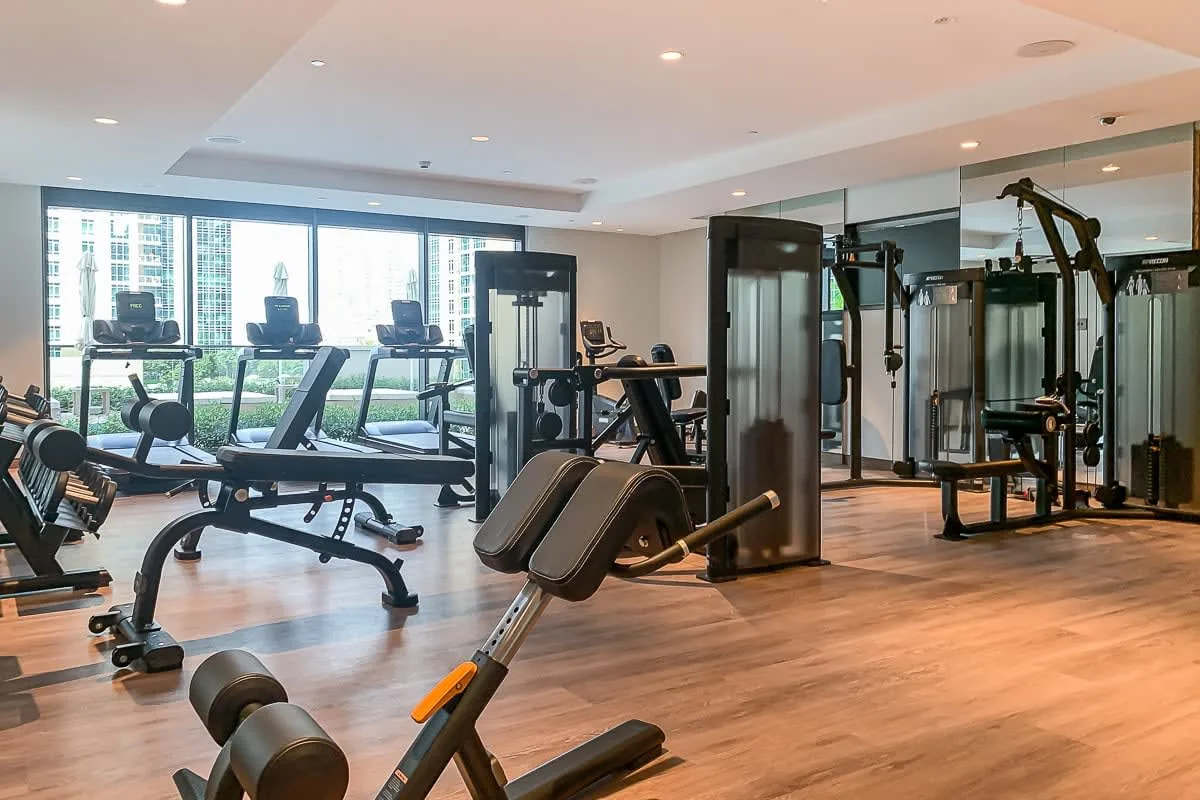 Una sala de ejercicio con máquinas y grandes ventanas con vista a edificios.