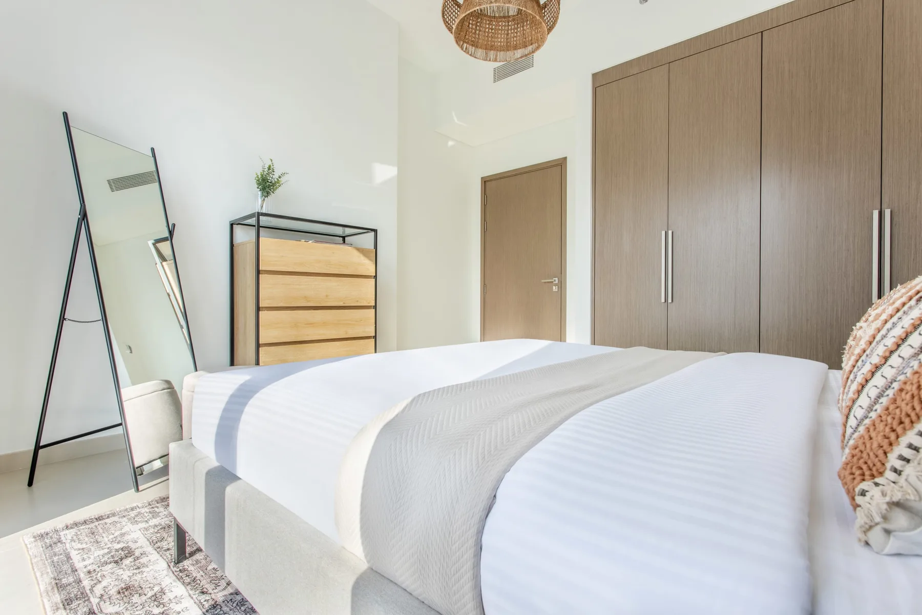 Dormitorio con una cama bien tendida, un espejo de pie y un armario de madera.