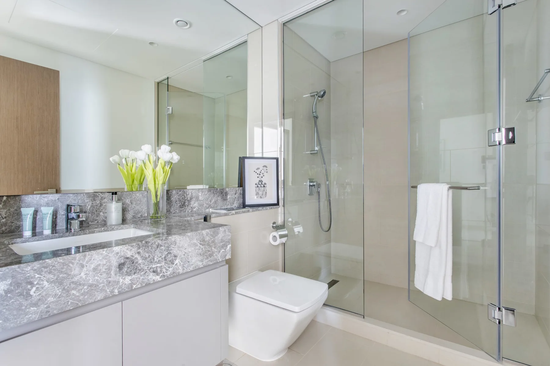 Un baño luminoso con lavabo, inodoro y ducha de vidrio.