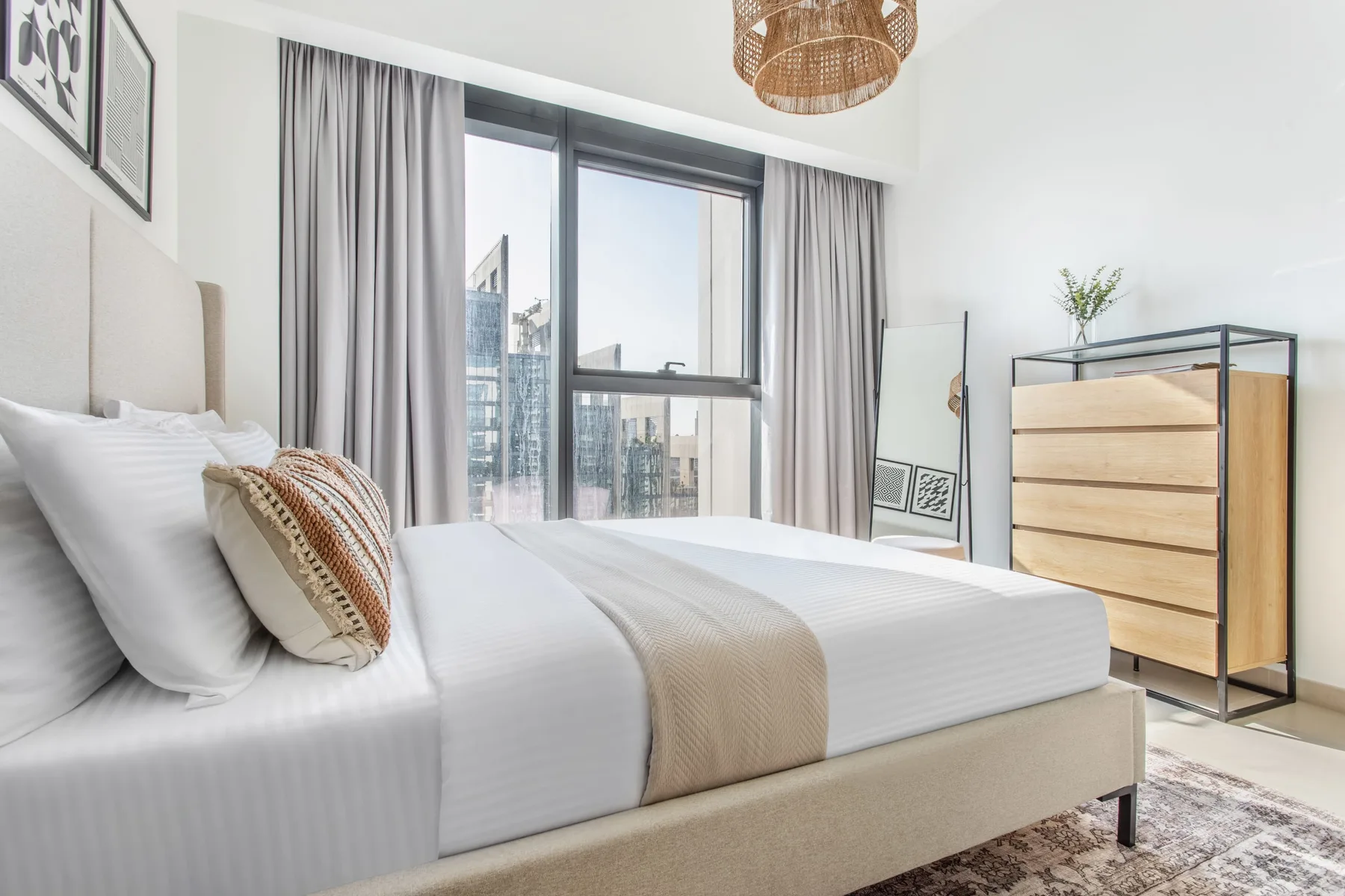 Un dormitorio luminoso con una cama bien arreglada junto a una ventana grande.