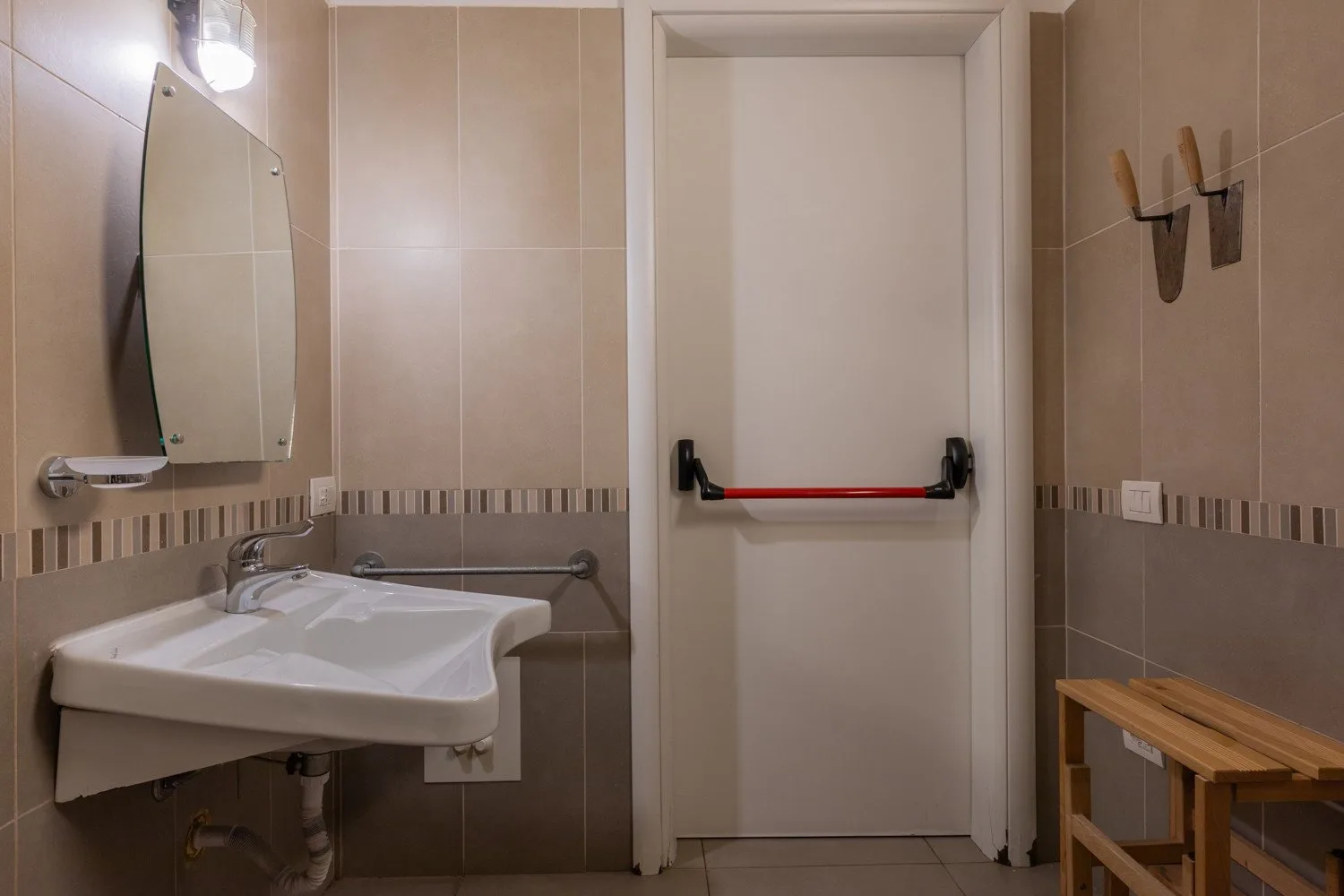 Un baño con azulejos, lavabo, espejo de pared y puerta cerrada.