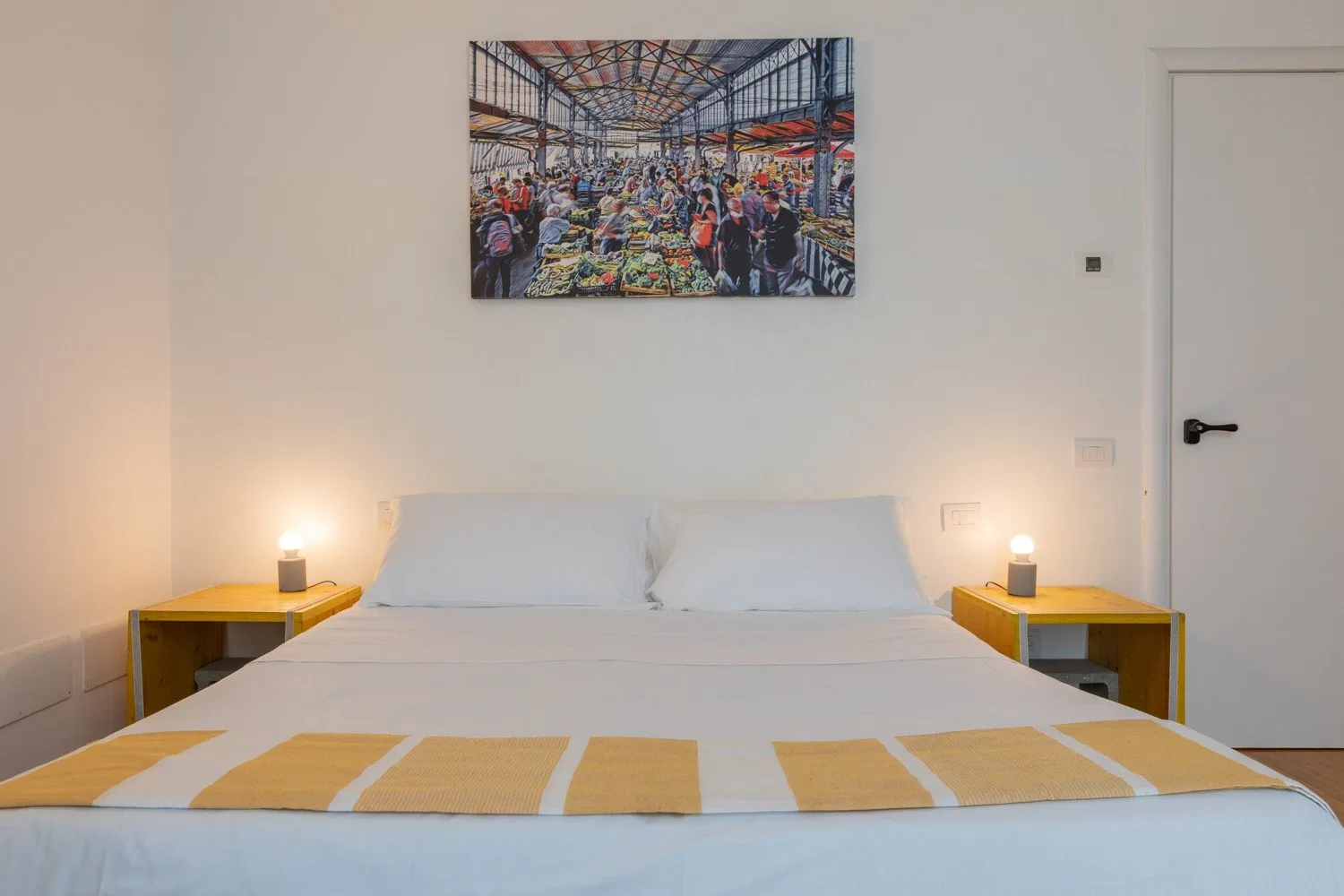 Un dormitorio con una cama bien tendida, mesas de noche y arte colorido en la pared.