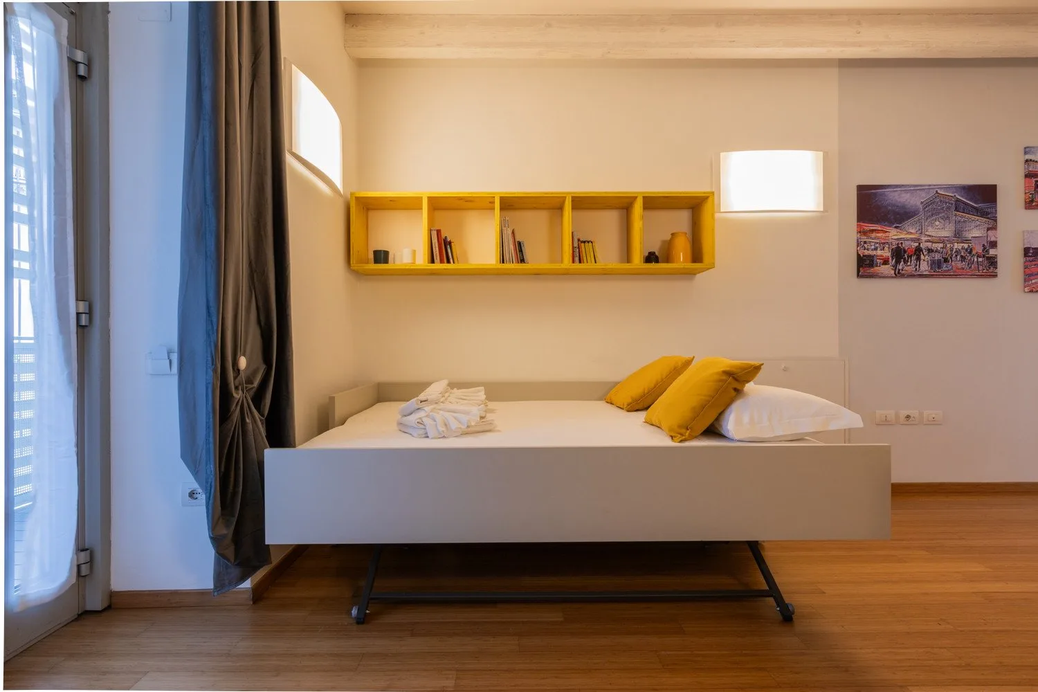 Un dormitorio con una cama elevada, almohadas amarillas y un estante de pared.