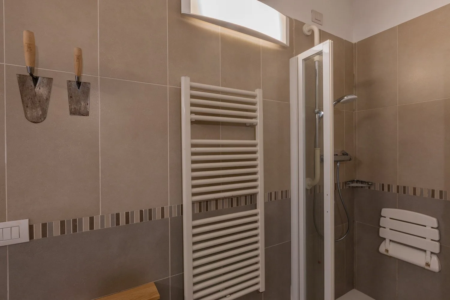 Un baño alicatado con radiador toallero mural y ducha.