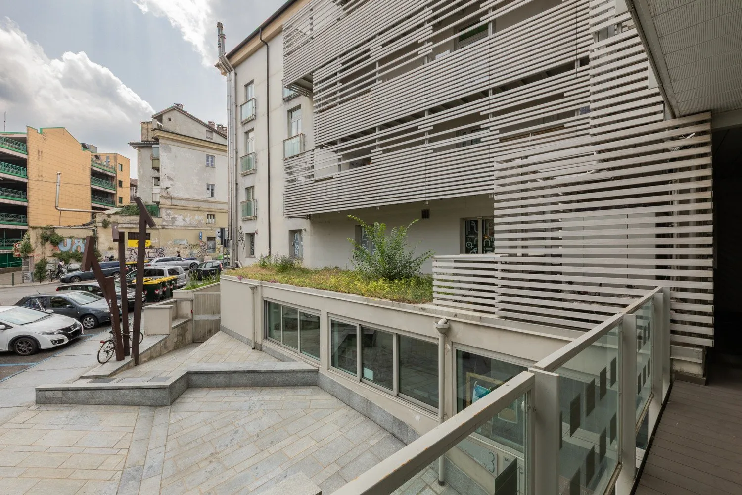 Exterior de edificio moderno con fachadas de listones horizontales y una terraza pavimentada.