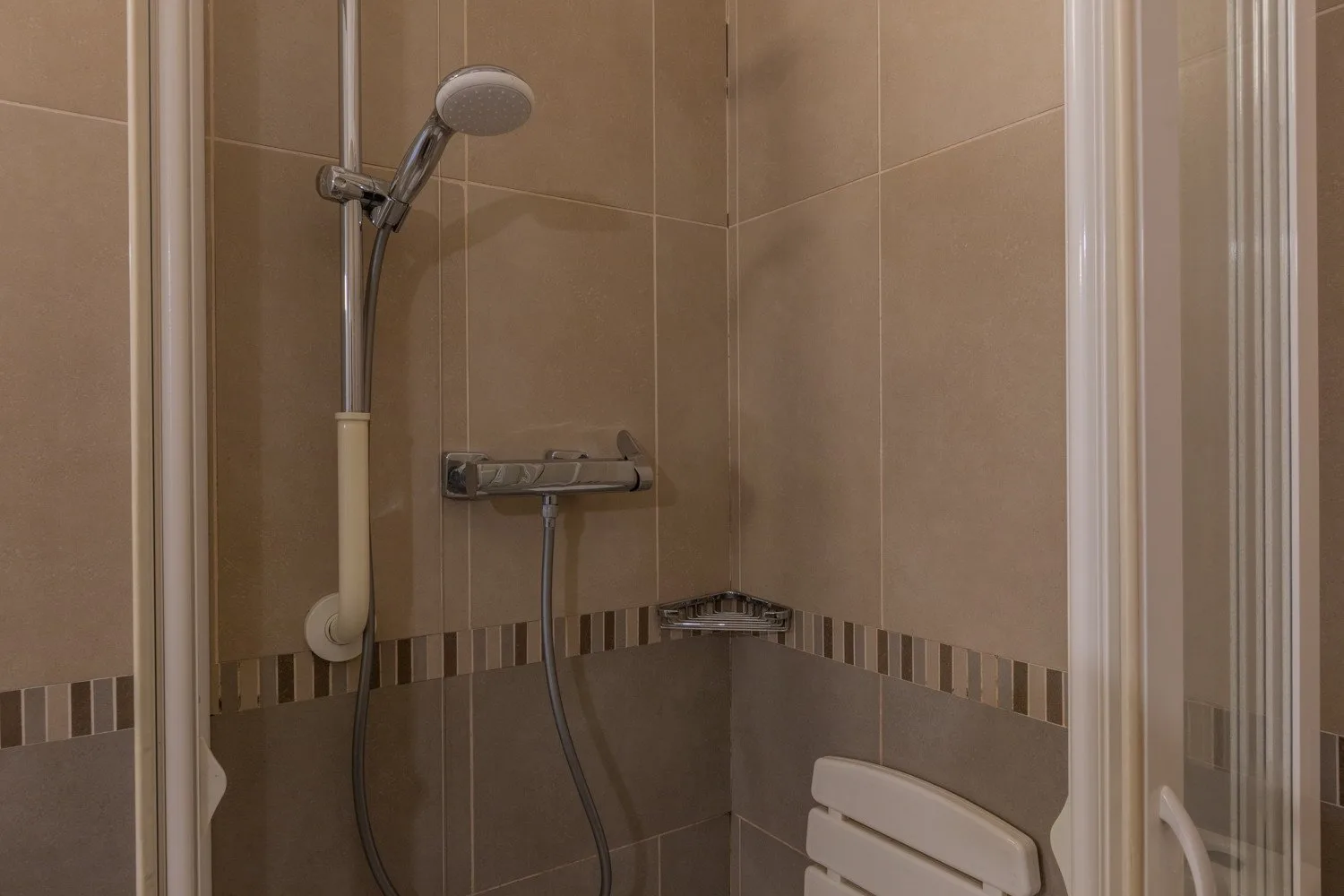 Una ducha con azulejos, ducha de mano y controles montados en la pared.