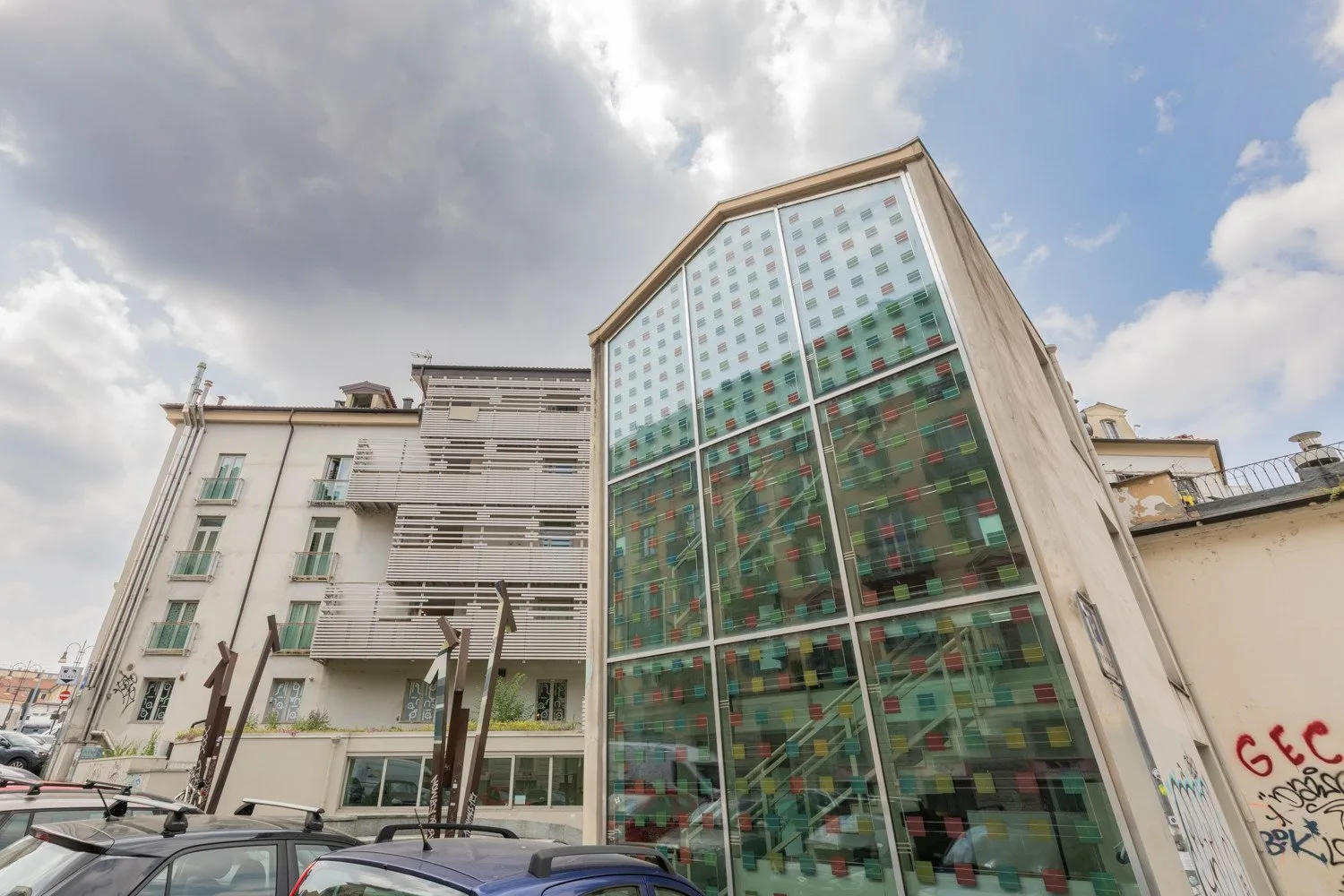 Un edificio moderno con fachada de vidrio está junto a un edificio claro de varias plantas.