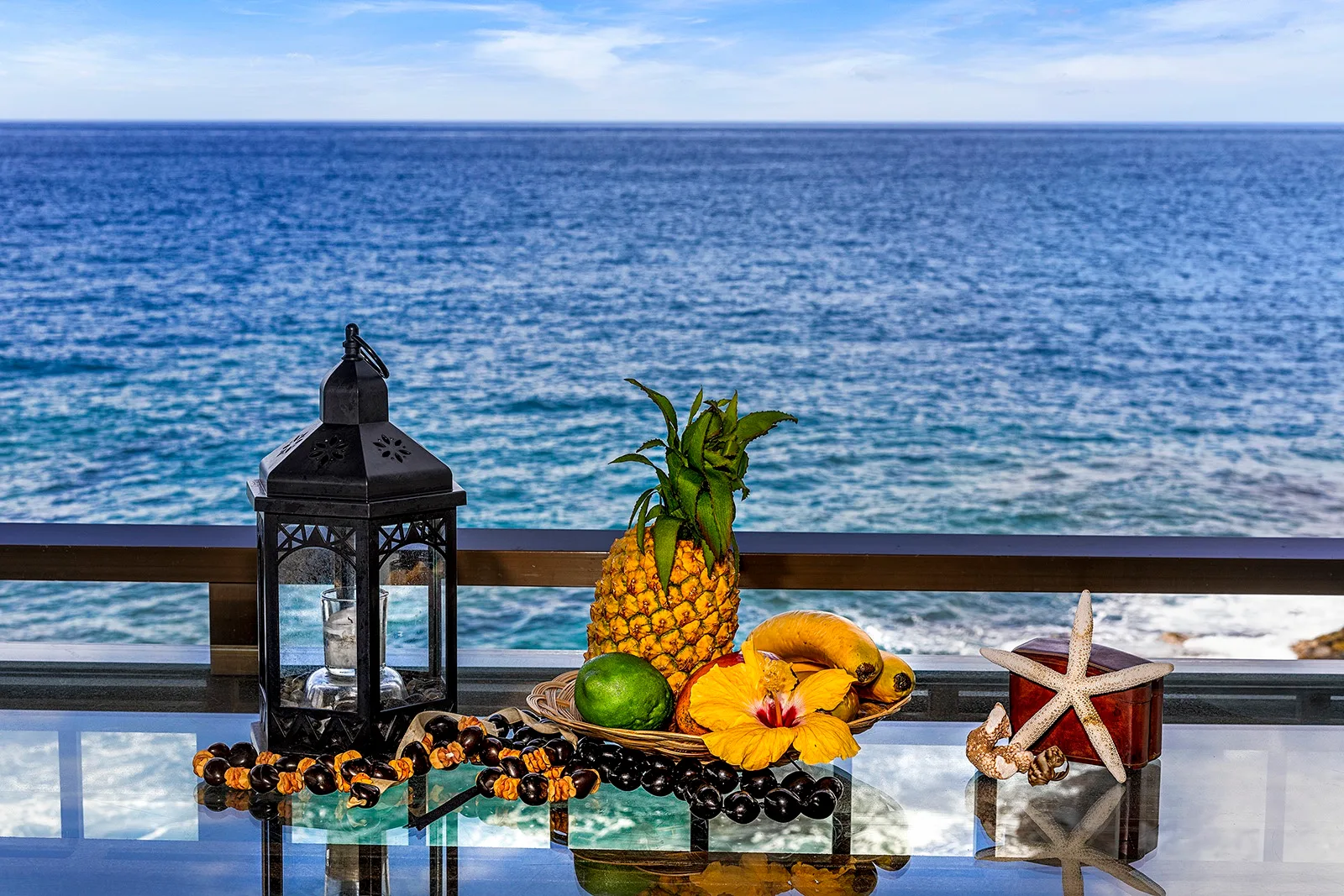 Una mesa junto al mar muestra frutas tropicales, un farol y una estrella de mar.