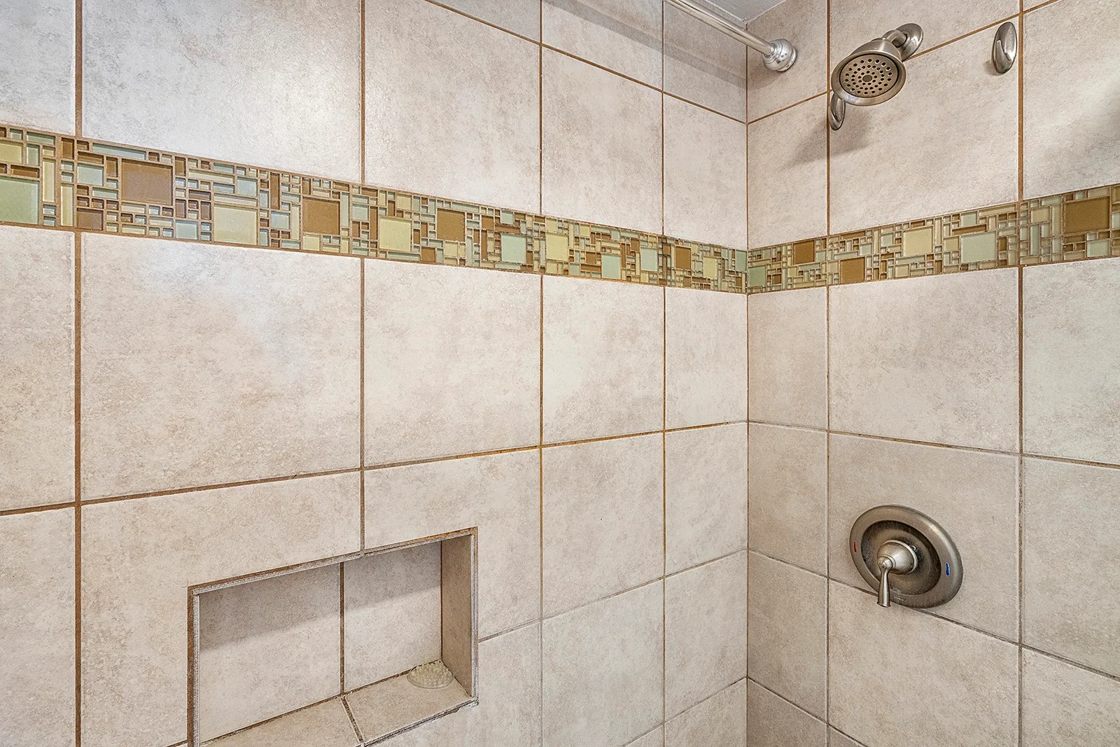 Una ducha con azulejos, una cenefa decorativa horizontal y un nicho empotrado.