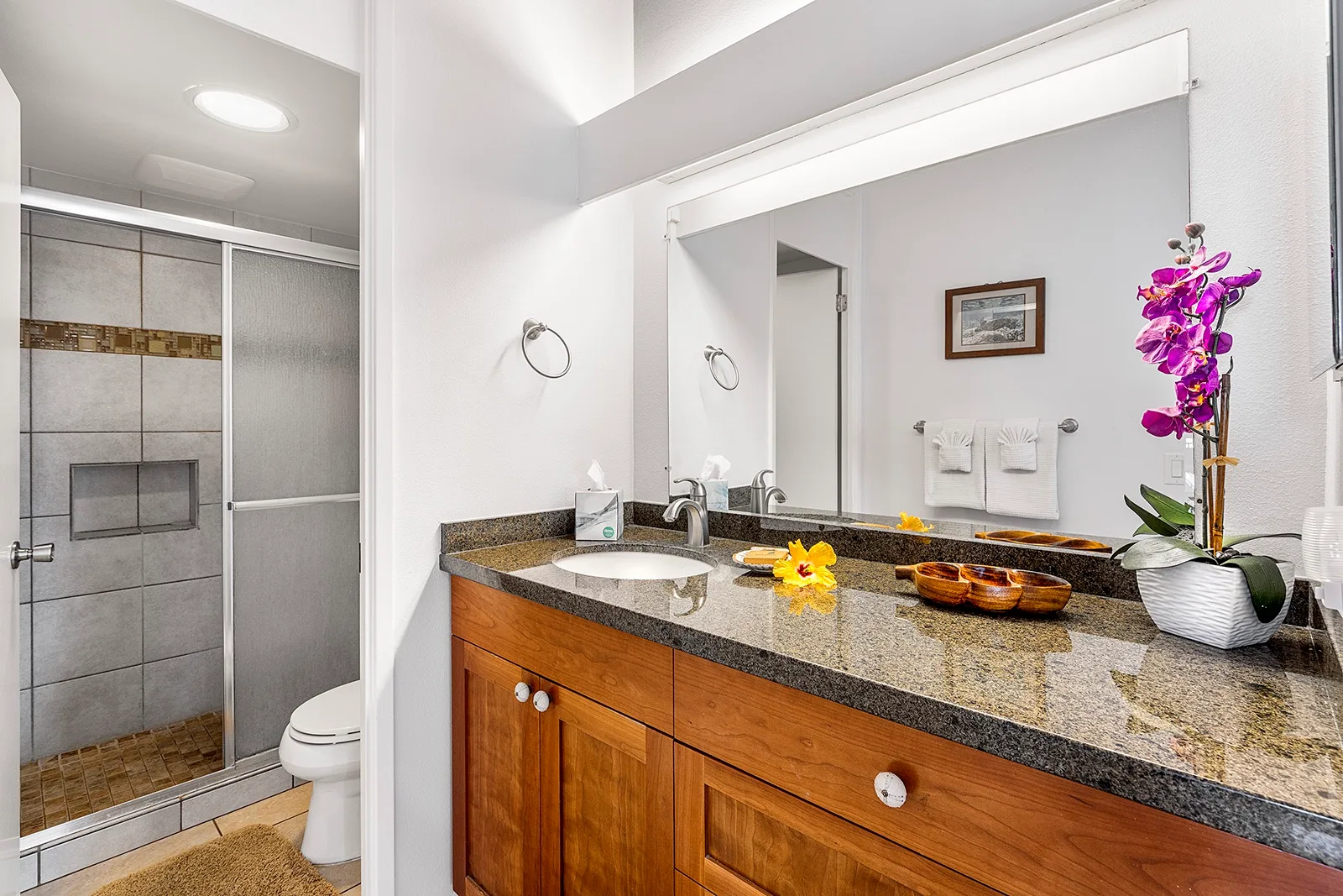 Un lavabo de baño con un espejo amplio junto a una ducha de azulejos.