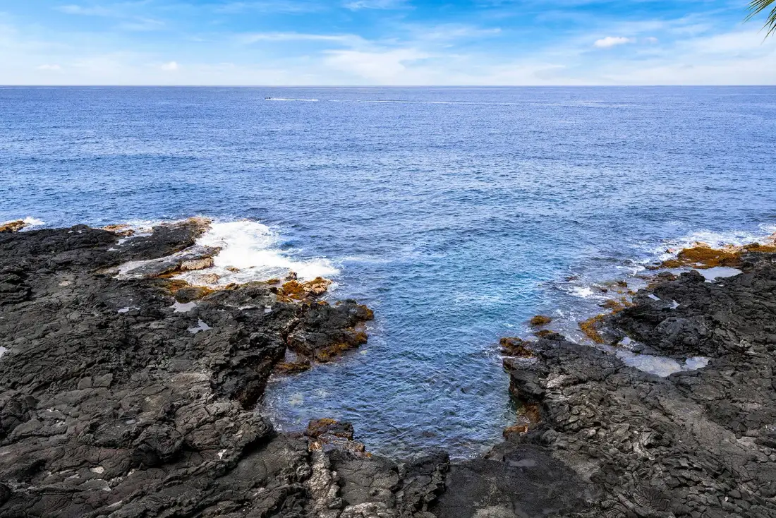 Una costa rocosa bordea el agua azul y clara del océano bajo un cielo parcialmente nublado.