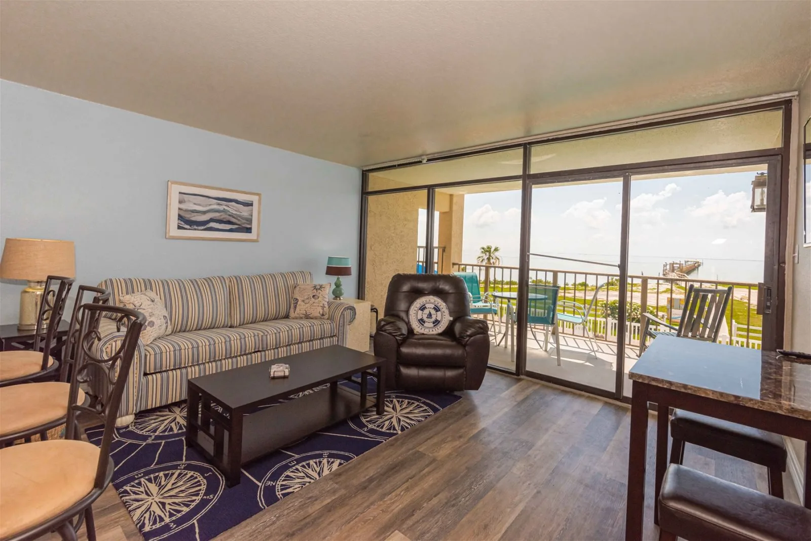 A living room with patterned seating, a coffee table, and sliding glass doors opening onto a balcony.