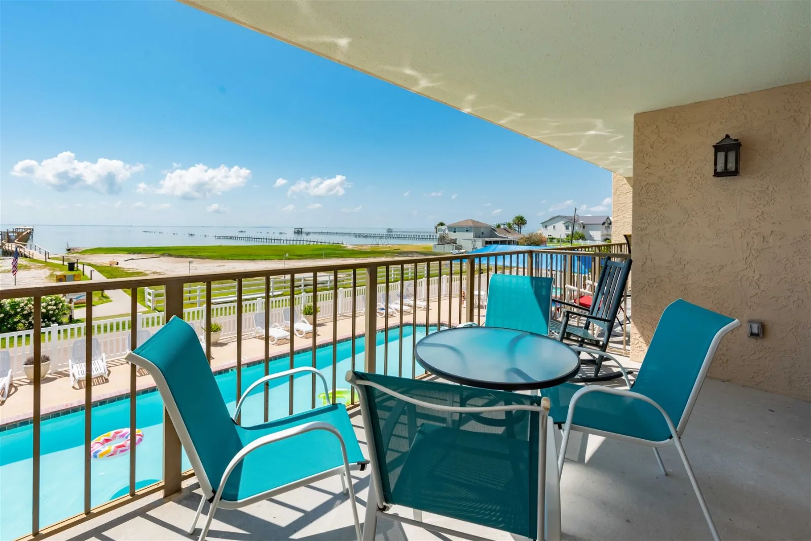 A balcony seating area overlooks a swimming pool and the waterfront.