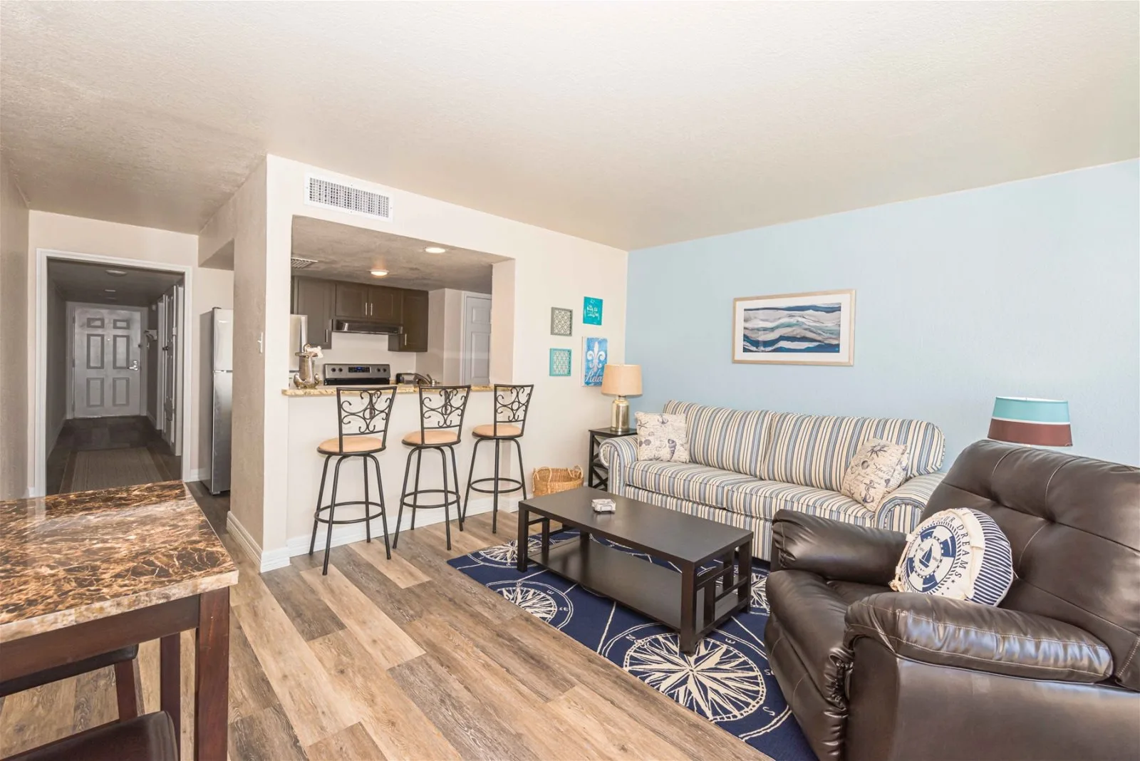 A living room with seating, a coffee table, and an open kitchen bar.