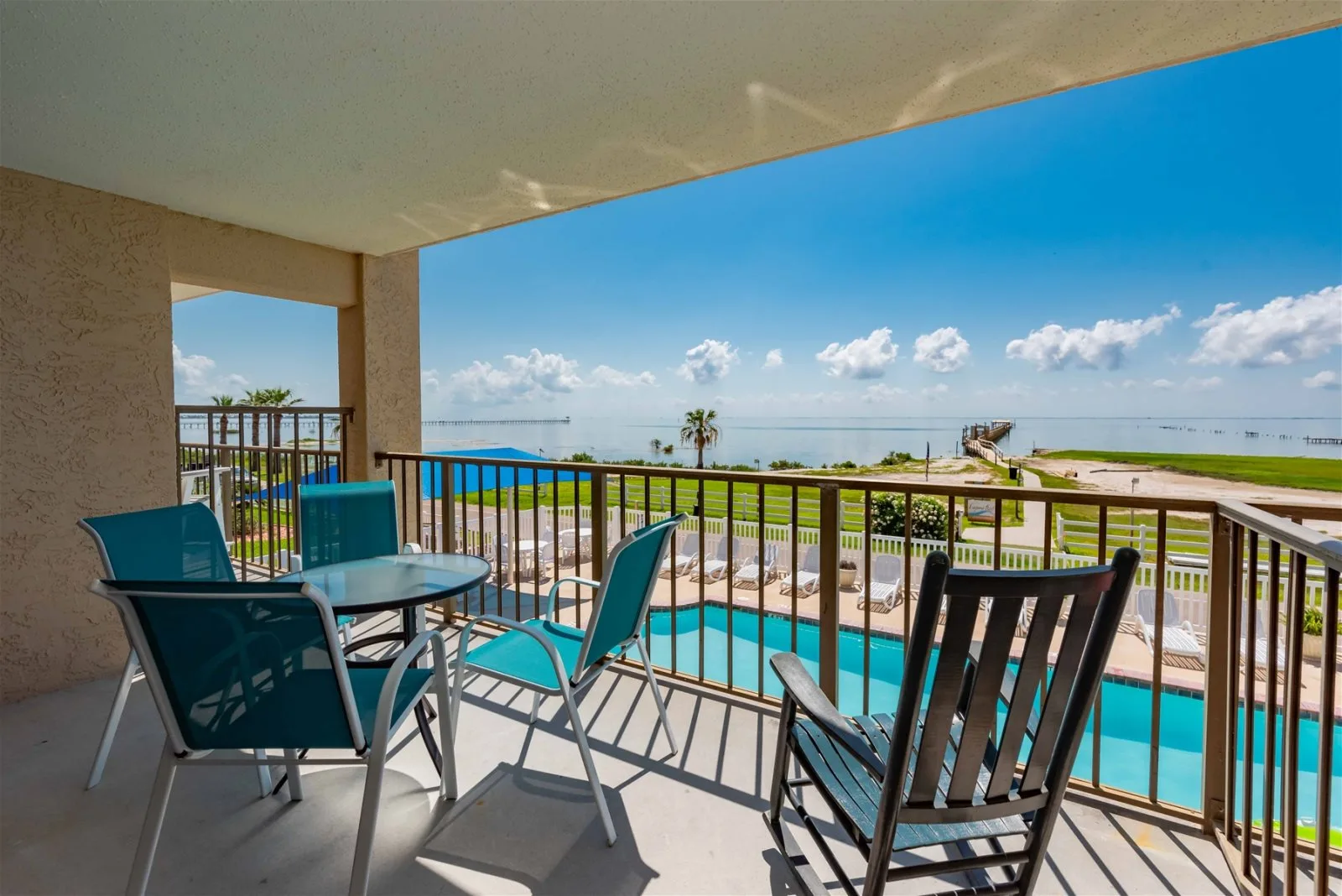 A covered outdoor seating area overlooks a pool and the ocean.