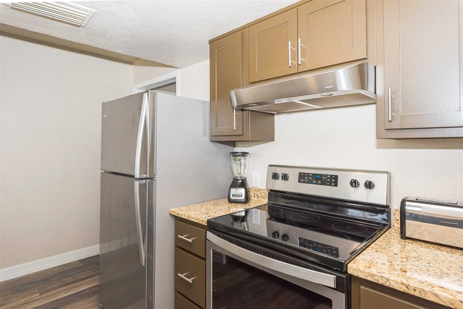 A kitchen with a stainless steel refrigerator, range, and overhead cabinets.