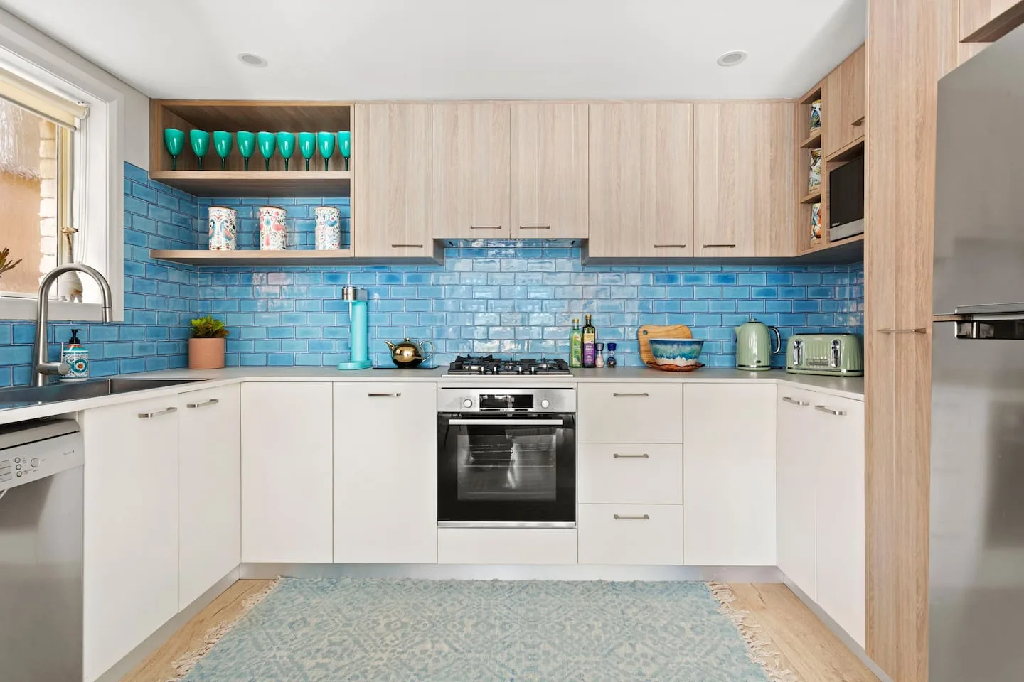 La cocina cuenta con una amplia superficie de trabajo para preparar comidas y un original revestimiento de azulejos azules que protege la pared de salpicaduras y aporta un toque divertido de color vibrante.