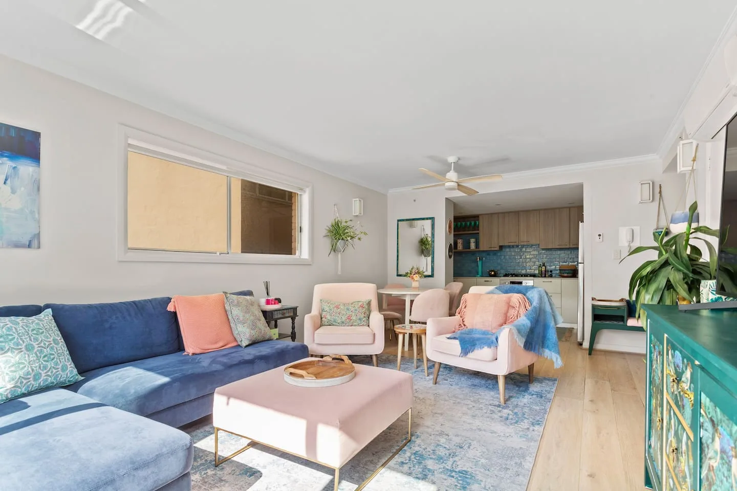 An open living area with a blue sectional, pink seating, and a kitchen in the background.