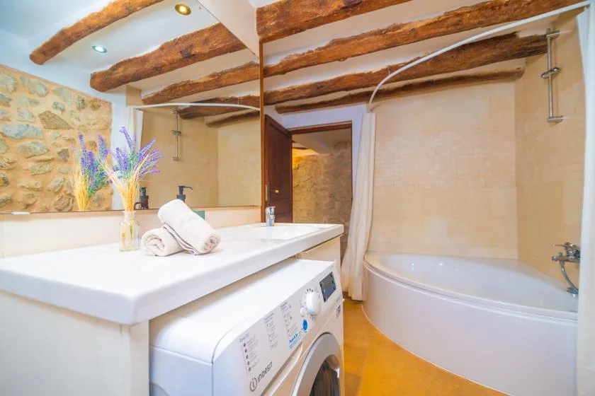 A bathroom with a bathtub, vanity, and washing machine beneath exposed wooden beams.