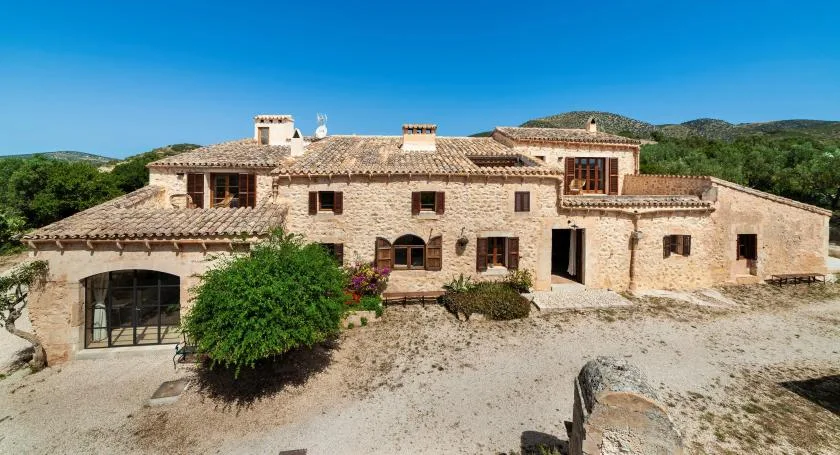 A stone house with tiled roofs stands in an open landscape.