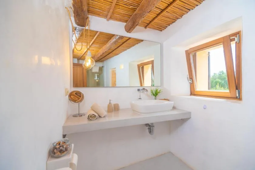 A bathroom vanity with a vessel sink sits beneath a large mirror and window.