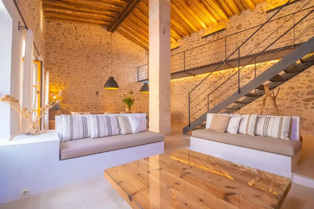 A spacious living room with seating beneath a wooden ceiling and beside a staircase.