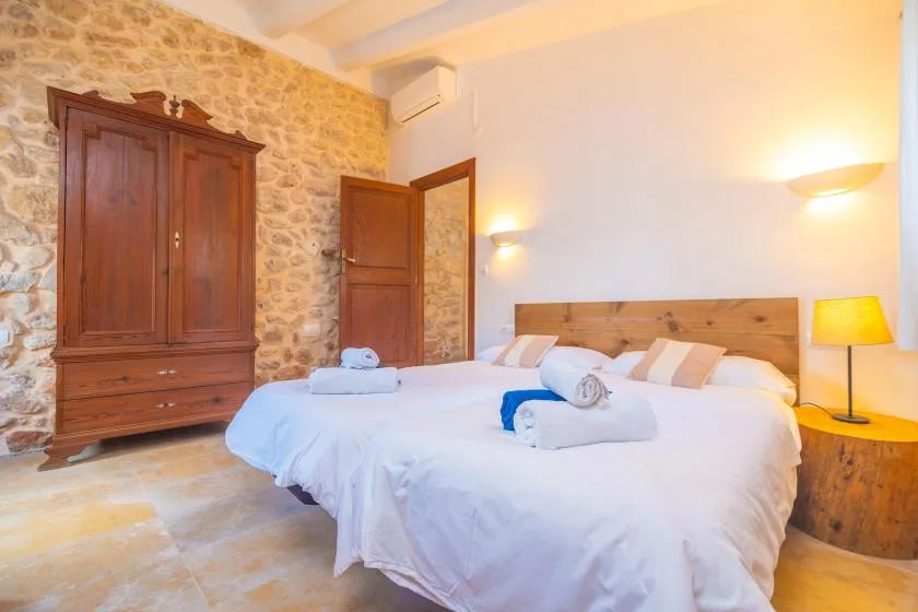 A bedroom with a large bed, wooden headboard, and stone wall.
