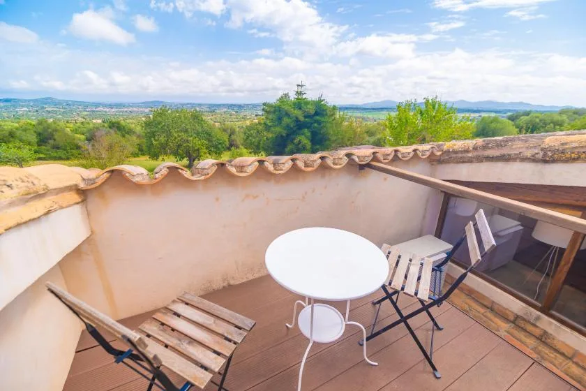 A rooftop terrace has a small table and seating overlooking a green landscape.
