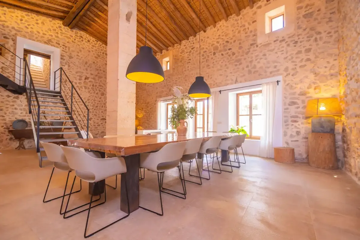A dining area with a long table and chairs beneath pendant lights.