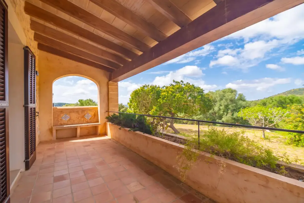 A covered terrace overlooks green fields and trees beneath a wooden roof.