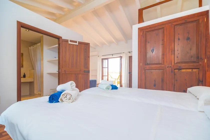 A bedroom with white bedding and wooden wardrobes beneath a sloped ceiling.