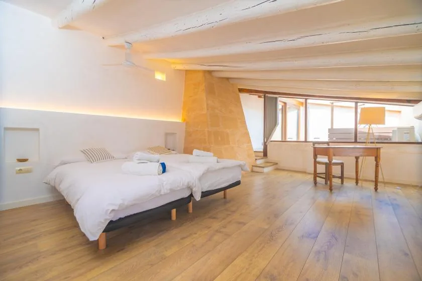 A bright bedroom with two beds and a small table beside the windows.
