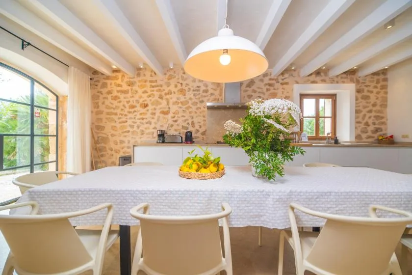 A dining area with a long table, white seating, and exposed stone walls.