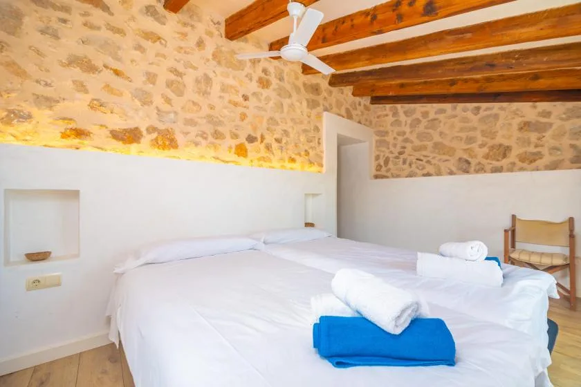 A bedroom with white bedding, exposed wooden ceiling beams, and stone walls.