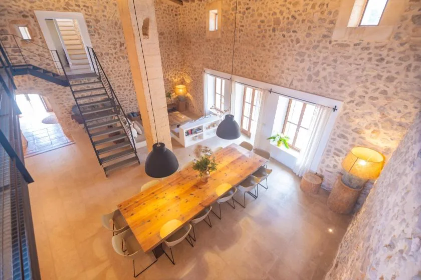 A stone-walled dining room with a long wooden table beneath hanging lights.