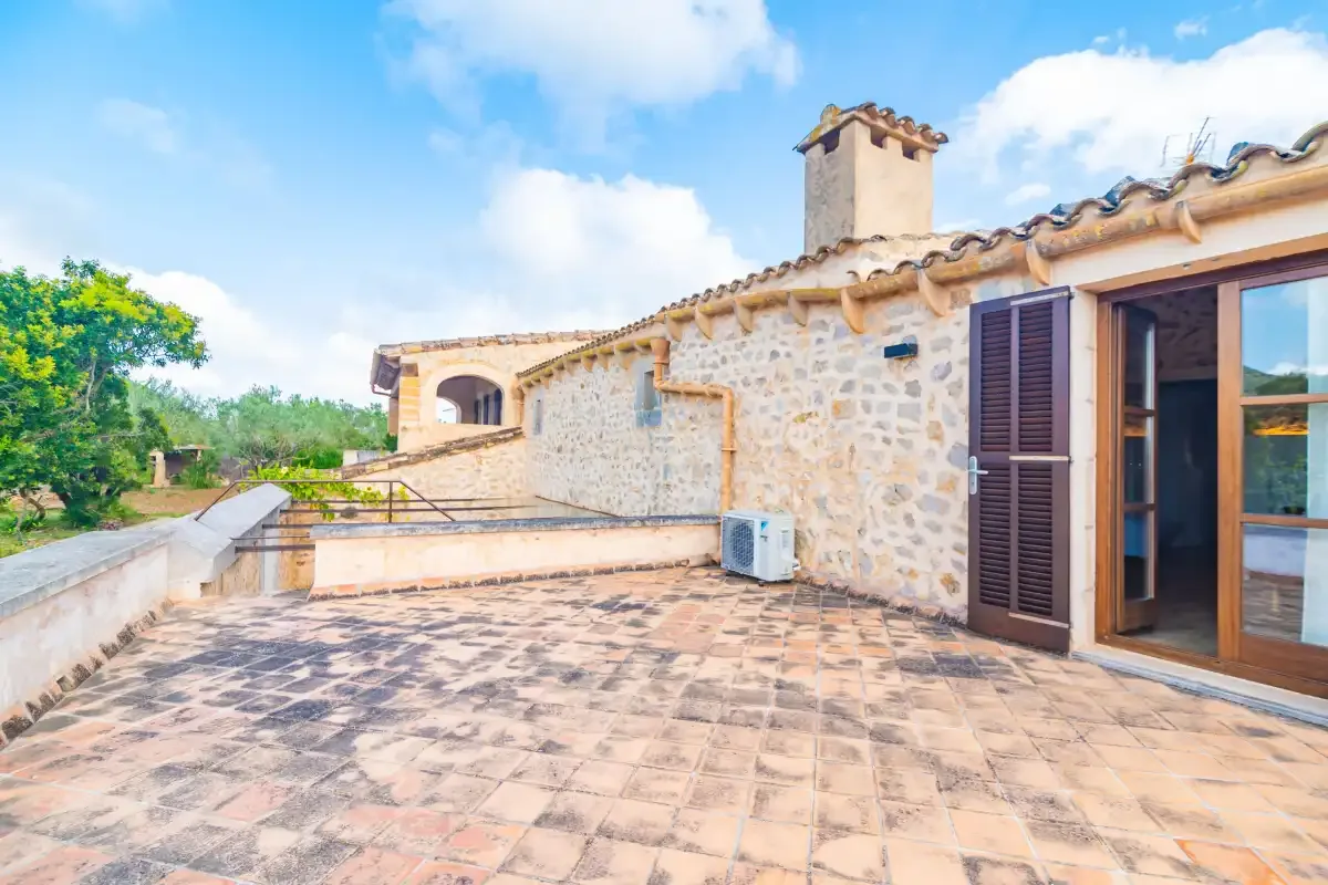 A tiled terrace beside a stone house opens onto a green landscape.