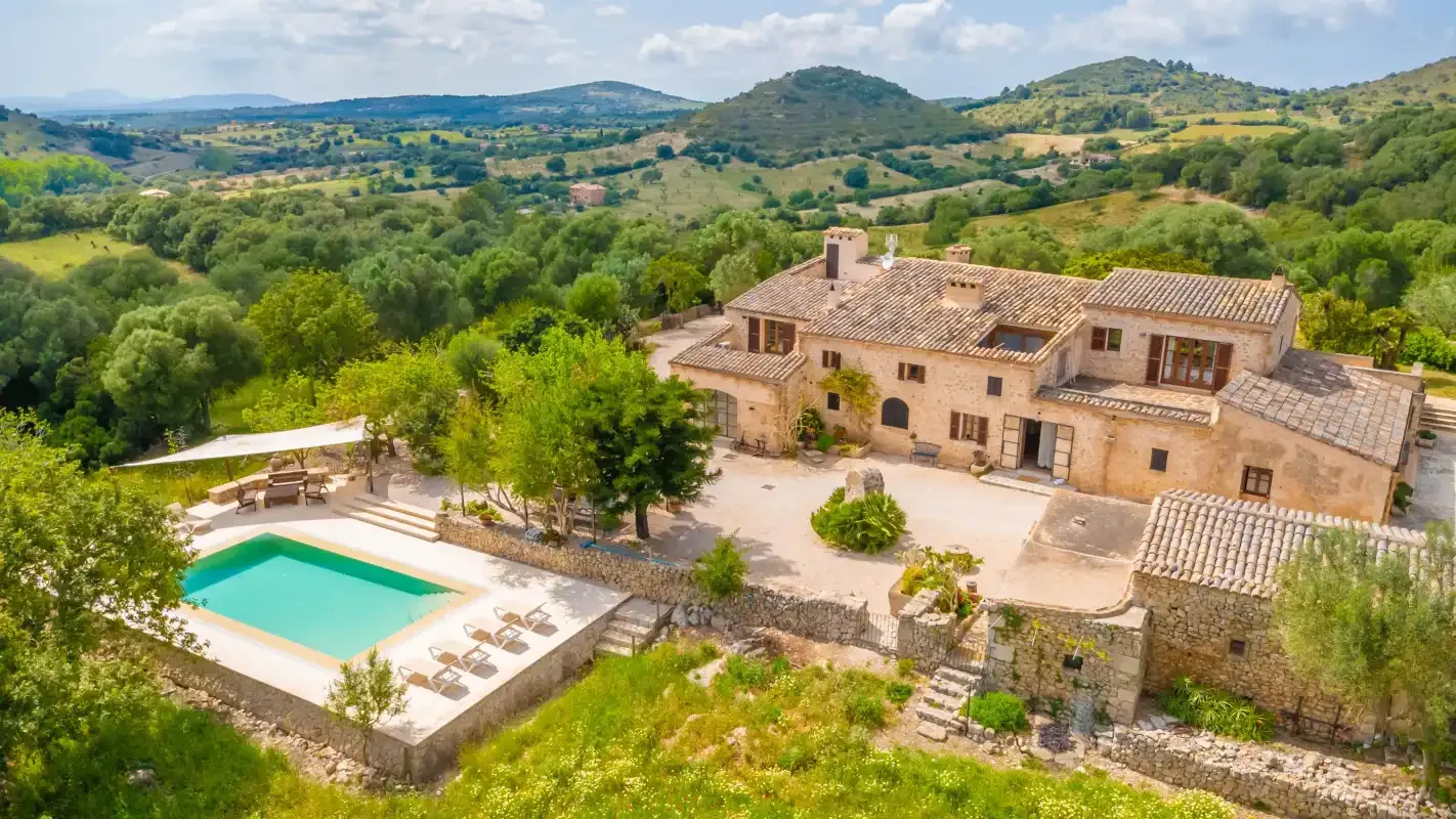 A stone house and swimming pool sit among green hills and countryside.