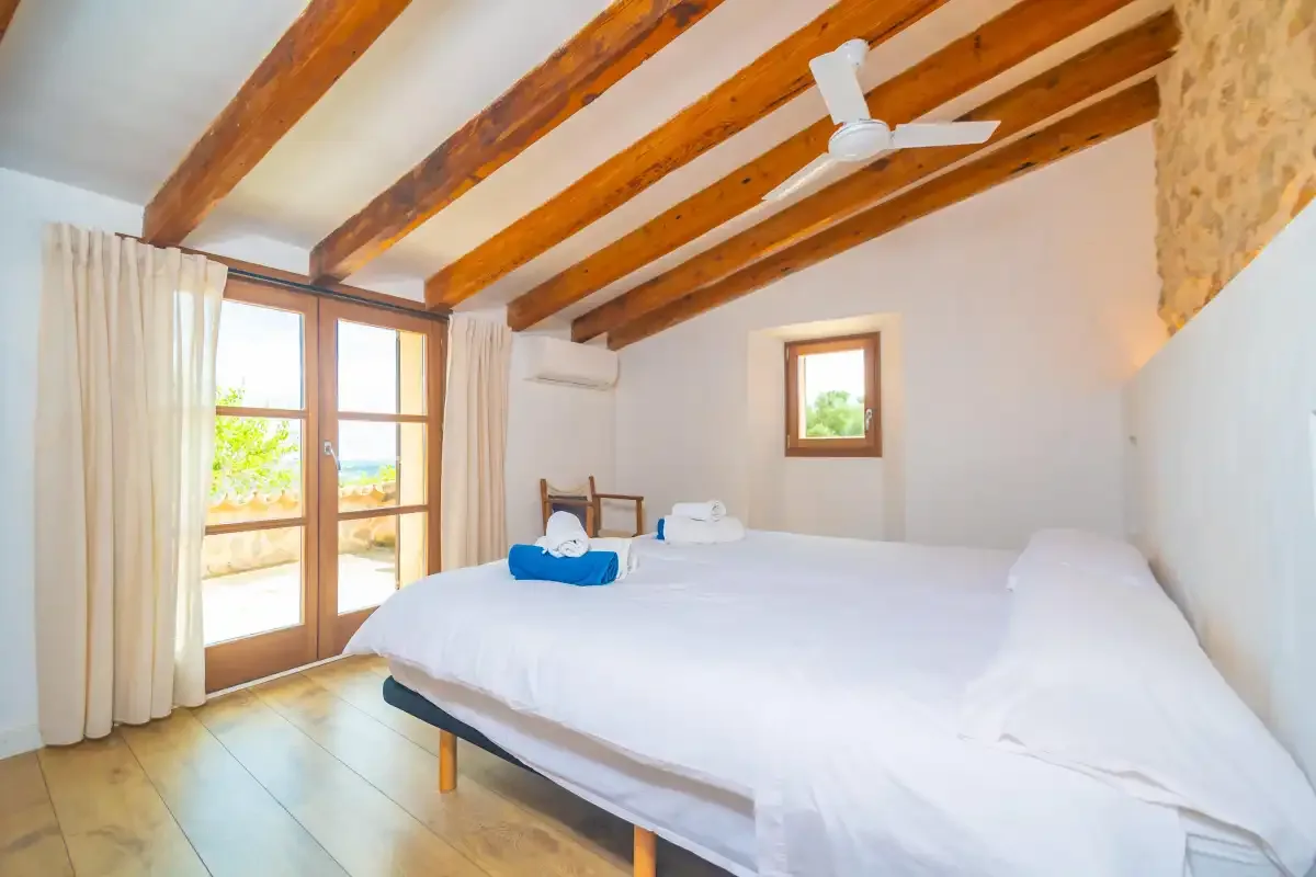 A bright bedroom with white bedding, exposed wooden ceiling beams, and a glass door.