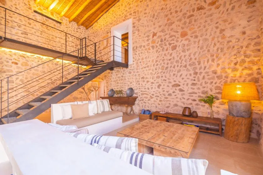 A rustic living room with a staircase, seating, and a wooden coffee table.