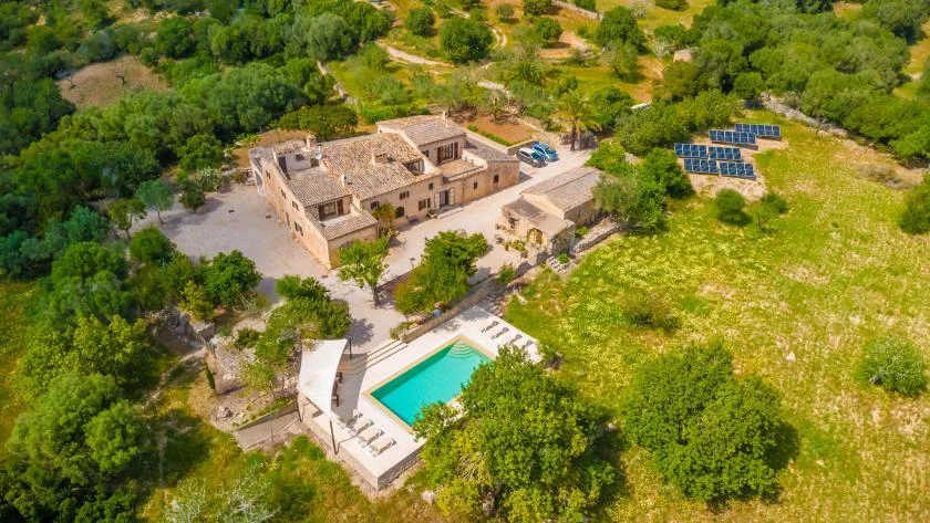 An aerial view of a stone building with a swimming pool amid green grounds.