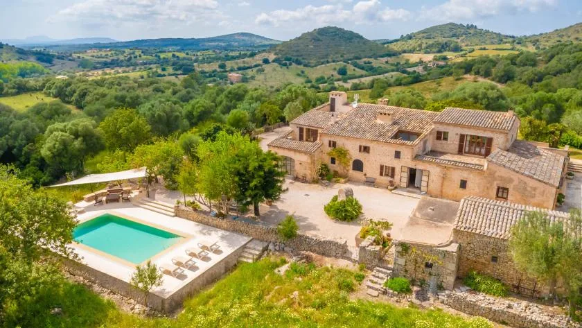 A countryside stone house and swimming pool overlook green rolling hills.