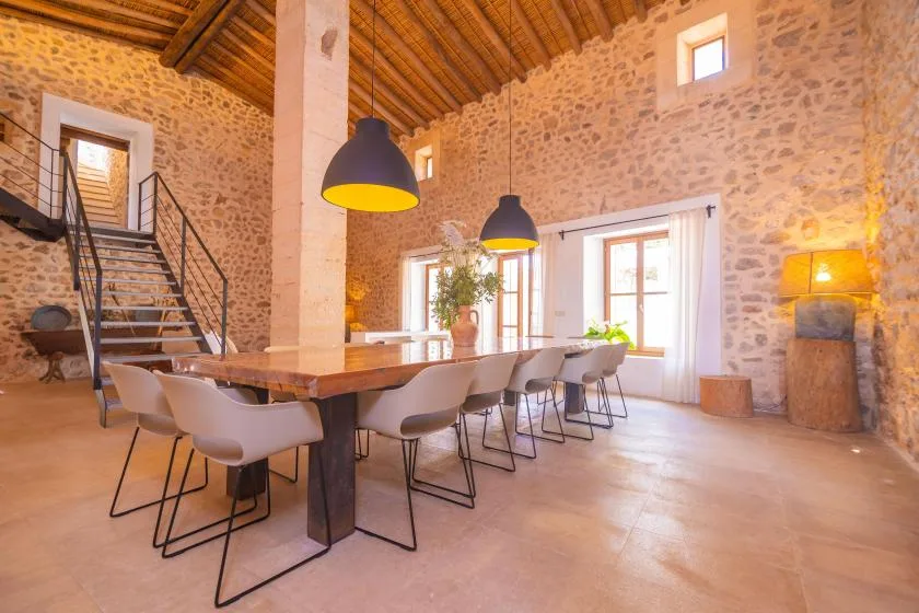 A rustic dining room features a long table beneath pendant lights.