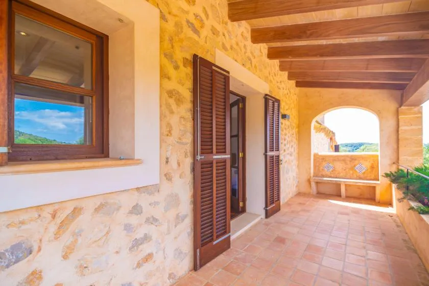 A covered stone terrace with wooden shutters and a distant landscape view.
